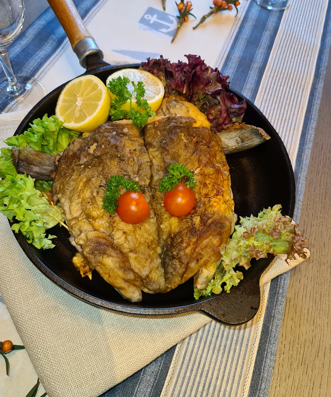 Frisch gebratener Kabeljaukopf in der Pfanne, mit Zitrone und Salat angerichtet